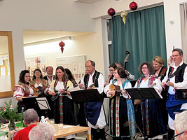 Eine Gruppe von Künstlern in traditioneller Kleidung singt und musiziert auf der Bühne.