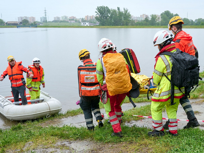 Zwei Rettungskräfte des Samariterbundes stehen in einem Schlauchboot und helfen vier weiteren Rettungskräften im Zuge einer Hochwasserübung, eine Person auf einer Trage in das Boot zu manövrieren.