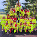 Gruppe von Personen in leuchtenden, gelben Arbeitsanzügen versammelt um einen Kletterbaum.
