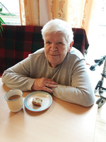 Eine ältere Frau sitzt an einem Tisch mit Kaffee und einem Stück Kuchen.