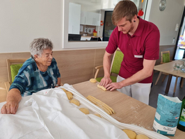 Ein junger Mann und eine ältere Frau bereiten gemeinsam Teig auf einem Tisch vor.