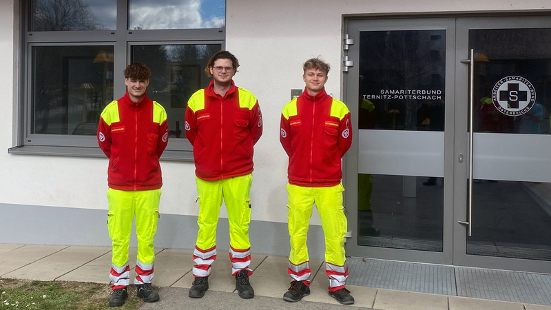 Drei Sanitäter stehen vor der Rettungsstelle in uniformierten Outfits.