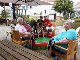 Senioren sitzen um ein kleines Planschbecken im Freien und genießen gemeinsame Zeit.