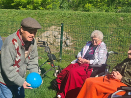 Ältere Menschen genießen die Sonne im Freien, während ein Kind mit einem Ball spielt.