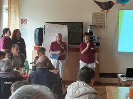Eine Präsentation in einem Raum mit Publikum und Vortragenden wird gehalten.