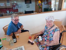 Ein älterer Mann und eine Frau in einem Rollstuhl sitzen gemeinsam an einem Tisch.