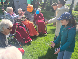 Eine Gruppe älterer Menschen spielt mit einem Kind Ball im Freien.