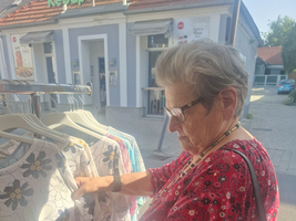 Eine ältere Frau betrachtet Kleidung an einem Kleiderständer.