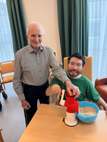 Ein älterer Mann und ein jüngerer Mann arbeiten gemeinsam mit einer Getreidemühle.