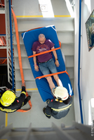 Feuerwehr trägt Patienten auf Trage im Stiegenhaus