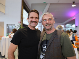Zwei lächelnde Männer stehen eng nebeneinander und posieren für ein Foto.