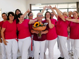 Eine Gruppe von Frauen in roten T-Shirts umarmt eine Kollegin mit Blumenstrauß.
