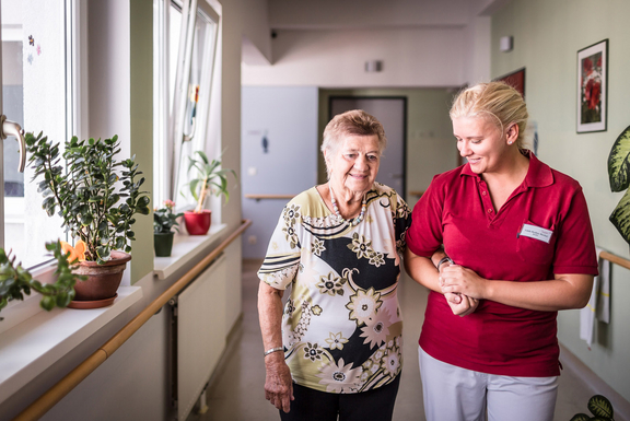 Altenpflegerin führt Bewohnerin eines Pflegekompetenzzentrums über den Gang