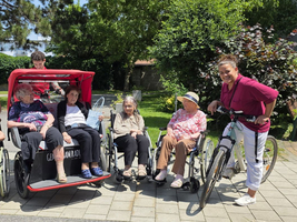 Gruppenszene mit älteren Menschen in Rollstühlen und Betreuern im Freien.