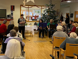 Weihnachtsfeier mit Musik und Reden in einem Gemeinschaftsraum für Senioren.