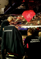 Zwei Personen in Helfer-T-Shirts sitzen in einer Veranstaltungshalle.