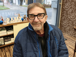 Ein älterer Mann mit Brille sitzt in einem Café, schaut lächelnd in die Kamera.