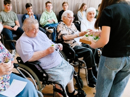 Jugendliche überreichen Senioren kleine Pflanzen in einem Gemeinschaftsraum.