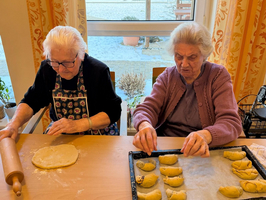 Zwei Frauen backen zusammen Teig und formen Plätzchen am Tisch.