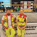 Zwei Rettungskräfte in Arbeitskleidung stehen vor einem Ring.
