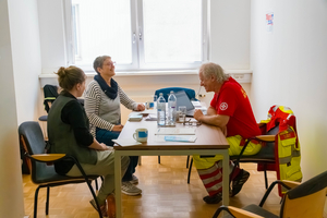 Drei Personen sitzen an einem Tisch und führen ein Gespräch.
