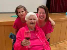 Drei Frauen in pinken Shirts posieren zusammen, eine hält ein Glas Rotwein.