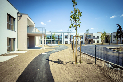 Neues Wohngebiet mit Weg, Bäumen und modernen Gebäuden unter blauem Himmel.