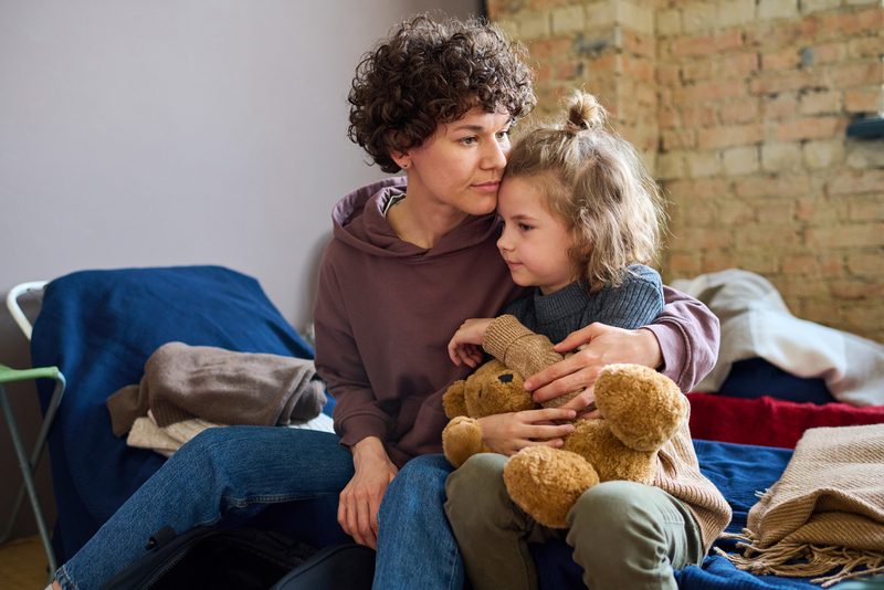 Eine Mutter und Ihre Tochter, die einen Teddybär in der Hand hält, sitzen auf einem Notbett,Familie , Armut, Wohnungslosigkeit