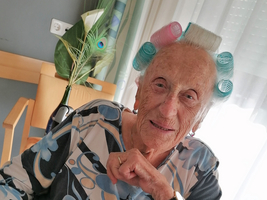 Eine ältere Frau mit Lockenwicklern lächelt in die Kamera.