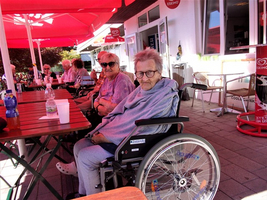 Ältere Frauen sitzen draußen an einem Tisch unter roten Sonnenschirmen.