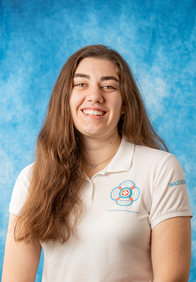 Lächelnde Person in weißem Polo-Shirt vor blauem Hintergrund.