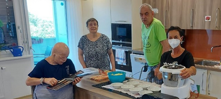 Gruppen von vier Personen in einer Küche, eine Person liest ein Buch.