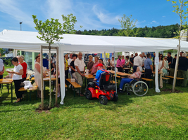 Menschen stehen und sitzen unter einem Zelt bei einer Veranstaltung im Freien.