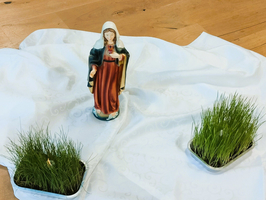 Eine Statue einer Frau umgeben von zwei Schalen mit Gras auf einem Tuch.