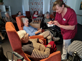 Pflegekraft zeigt einer Seniorin etwas während einer Gruppensitzung im Pflegeheim.