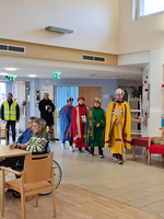Gruppe verkleideter Personen zieht durch den Raum, während Senioren zuschauen.
