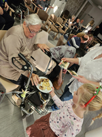 Eine ältere Frau sitzt im Rollstuhl und erhält von einem Kind einen Teller mit Keksen.