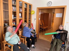 Drei Frauen im Raum halten bunte Schaumstoffstäbe und spielen zusammen.