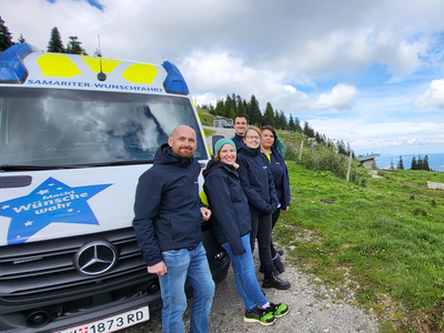 Eine Gruppe von fünf Personen steht neben einem Krankenwagen in der Natur.