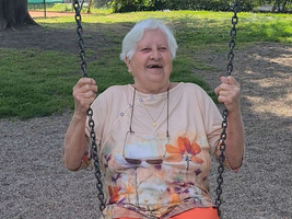 Eine ältere Frau sitzt lachend auf einer Schaukel im Park.