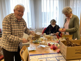 Drei Personen basteln gemeinsam mit verschiedenen Materialien an einem Tisch.