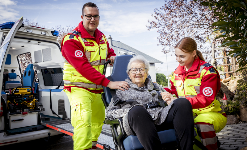 Zwei Sanitäter mit einer älteren Frau im Transportsessel des Krankentransports.