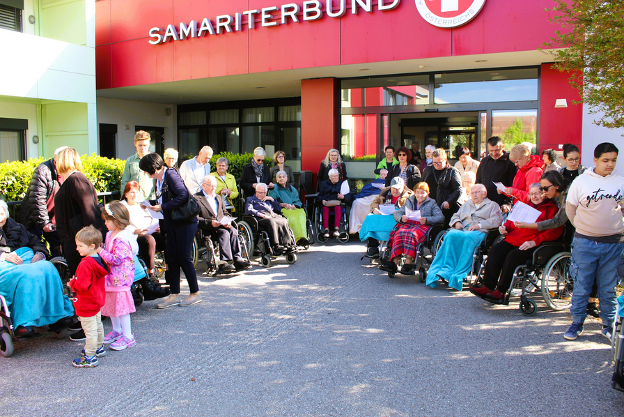 Eine Gruppe älterer Menschen, begleitet von Kindern, vor einem Gebäude des Samariterbundes.