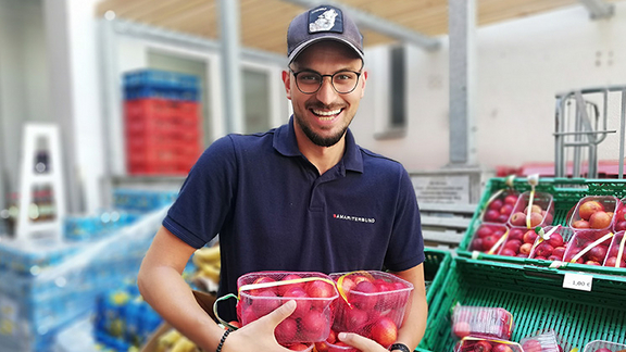 Mitarbeiter von Sozialmarkt lächelt in Kamera und hält verpackte Pfirsiche