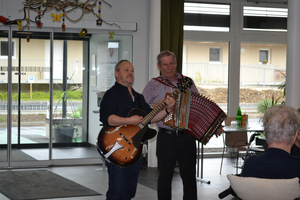 Zwei Musiker spielen gemeinsam Gitarre und Akkordeon in einem Raum.