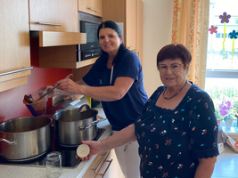 Zwei Frauen kochen gemeinsam in einer Küche mit Töpfen auf dem Herd.