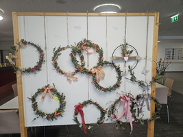 Dekorative Kränze aus Blumen und Bändern an einer Wand präsentiert.