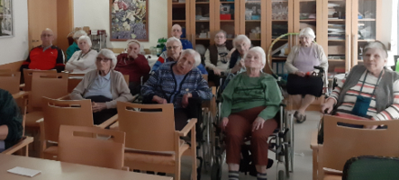 Einige ältere Menschen sitzen in einem Raum und hören aufmerksam zu.
