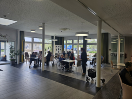 Menschen sitzen und interagieren in einem hellen Gemeinschaftsraum.