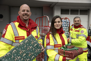 Drei Personen in Uniform halten Geschenke vor einem Lagerhaus.